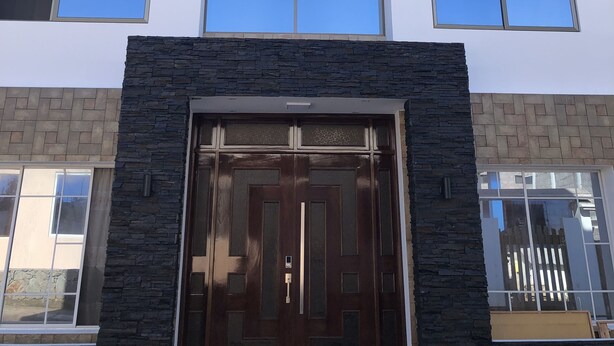 Un edificio moderno con múltiples ventanas, una entrada central con puerta de vidrio y paredes con textura de piedra.