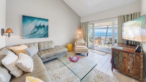 Una sala de estar con un sofá, sillones, una mesita de centro y vista al mar a través de un ventanal.