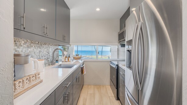 Una cocina moderna con gabinetes grises, un refrigerador de acero inoxidable y una ventana con vista a la playa.