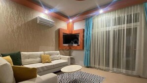Un salón con un sofá blanco, un tapete estampado y un televisor instalado en una pared naranja.
