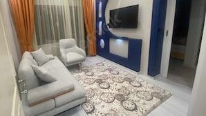 Una sala de estar con un sofá, sillones, un tapete estampado y un televisor de pantalla plana montado en la pared.