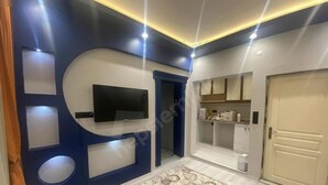 Un pasillo de diseño moderno, con un televisor de pantalla plana montado en la pared, un tapete estampado y una puerta que da a una habitación con armarios y encimera.