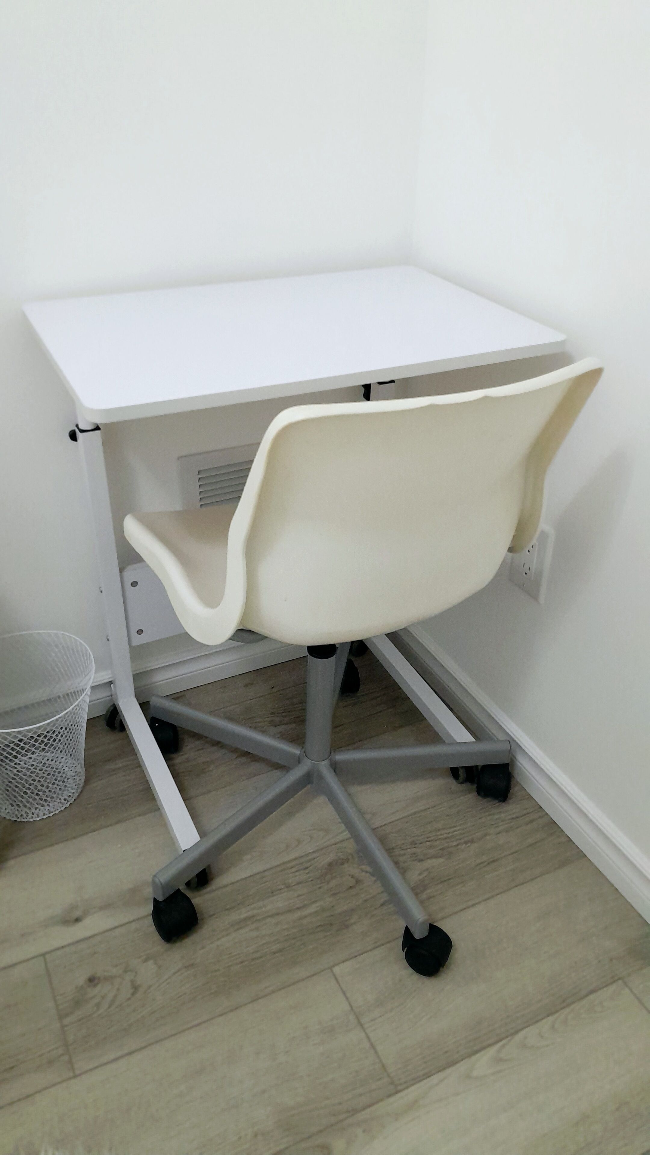 Un bureau blanc dont le bord avant est incurvé, avec une poubelle en treillis placée à côté.