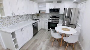 A modern kitchen with white cabinets, stainless steel appliances, and a round dining table with chairs.