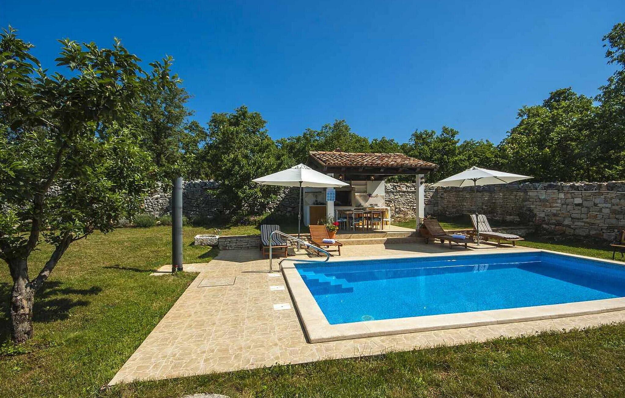 A backyard with a swimming pool, outdoor seating, and a stone wall.