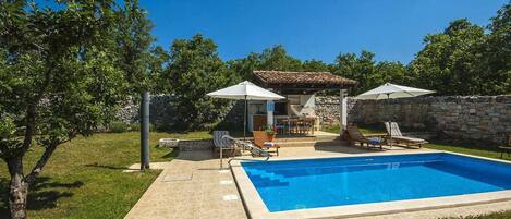 A backyard with a swimming pool, outdoor seating, and a stone wall.