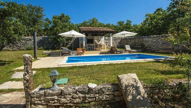 Ein Garten mit Schwimmbad, Steinmauern und Gartenmöbeln.