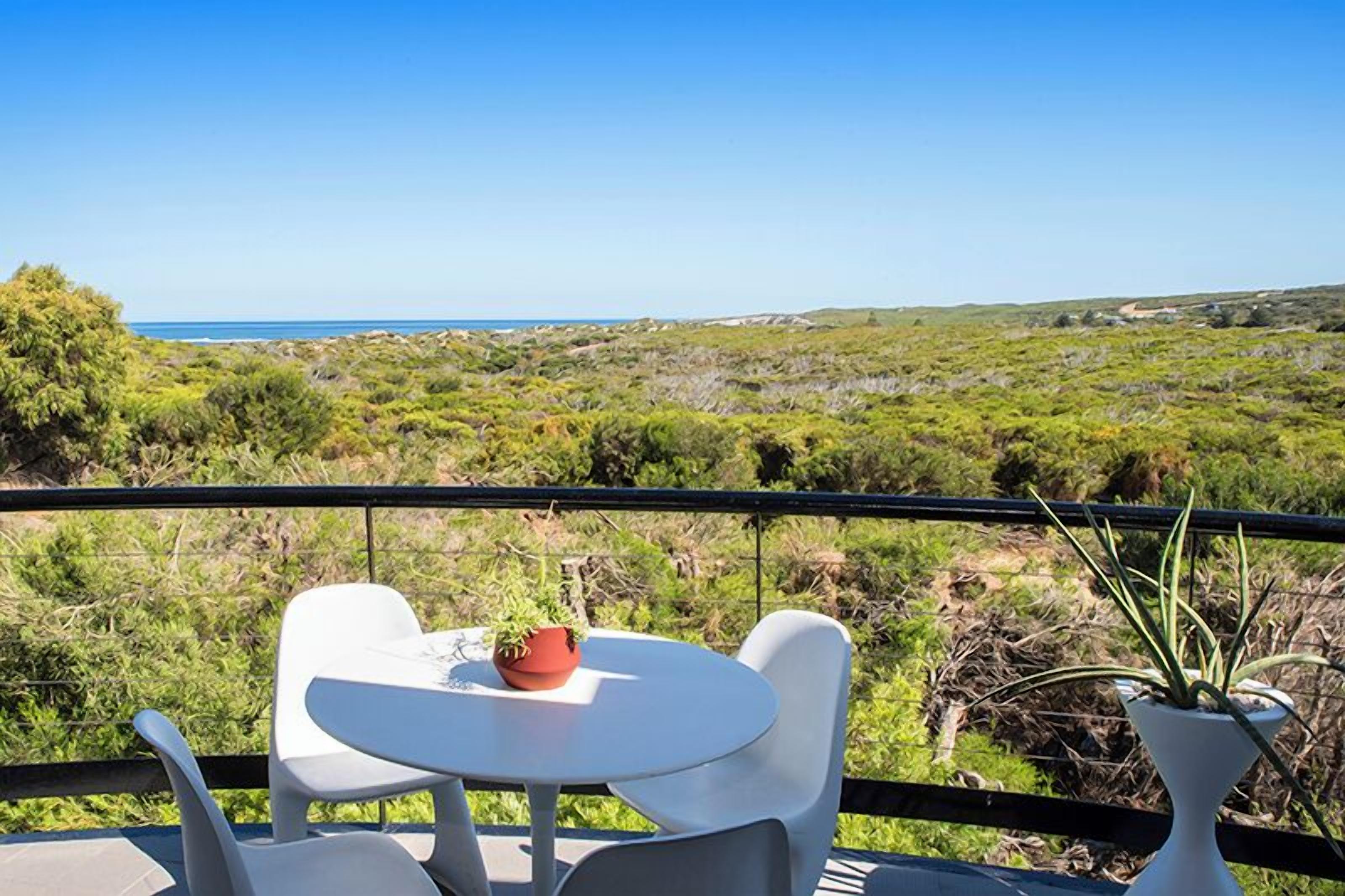 A terrace with a table and chairs, overlooking a coastal landscape.