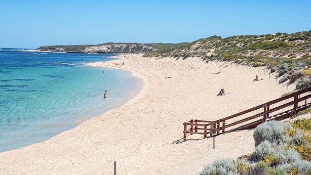 En strand med klart, blått vatten, en sandstrand och ett trästaket.