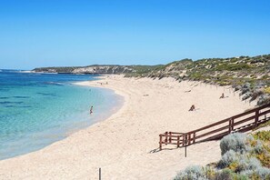A beach with clear blue water, sandy shore, and a wooden fence.