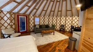 A yurt interior with a sofa, coffee table, and a small kitchen area. - Gray Yurt in Hocking (Logan)