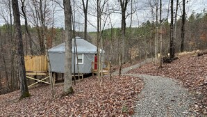 A cabin with a gray roof and a red door, surrounded by trees and a gravel path. - Gray Yurt in Hocking (Logan)