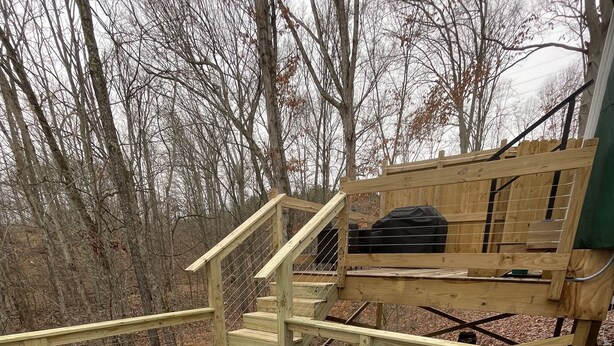 A hot tub on a wooden deck with a wooden staircase and a bench in the background. - Gray Yurt in Hocking (Logan)
