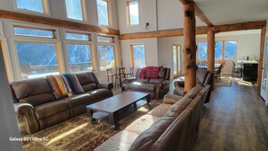 A spacious living room with leather sofas, a coffee table, and a dining area with chairs and a table. Large windows provide natural light and views of the outdoors. - Amazing Mountain Getaway (Marble)