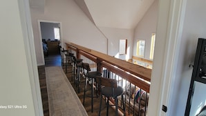 A high-ceilinged room with a wooden staircase, a long wooden bench with chairs, and a bed with a headboard. - Amazing Mountain Getaway (Marble)