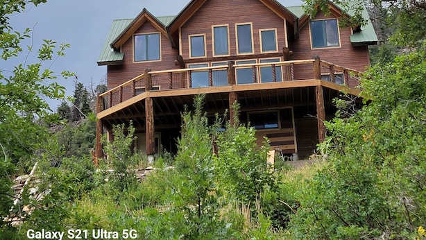 A large, multi-story wooden house with a balcony, surrounded by dense greenery. - Amazing Mountain Getaway (Marble)