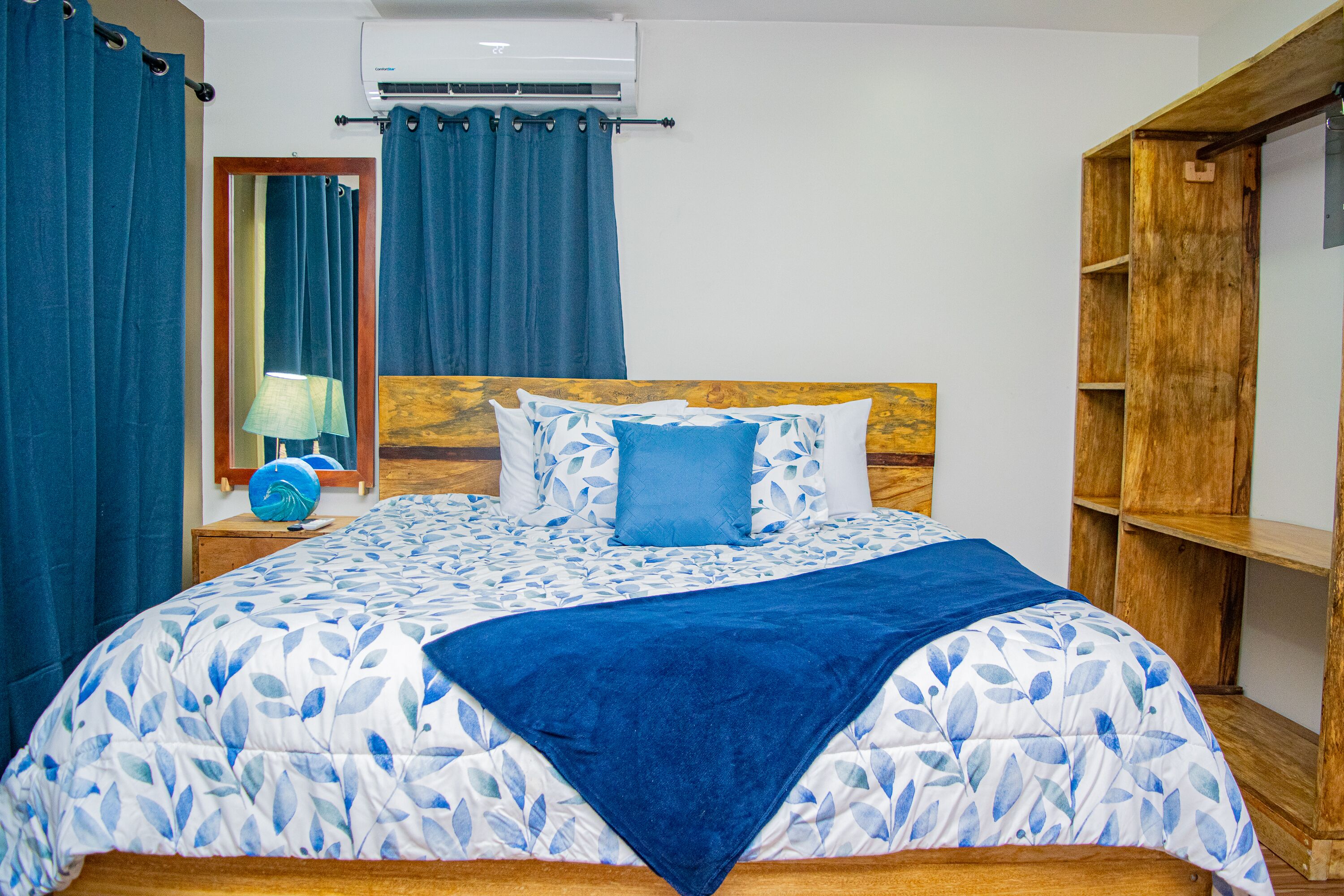 A bedroom with a bed, a wooden headboard, a nightstand with a lamp, and a blue curtain.