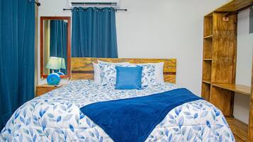 A bedroom with a bed, a wooden headboard, a nightstand with a lamp, and a blue curtain.