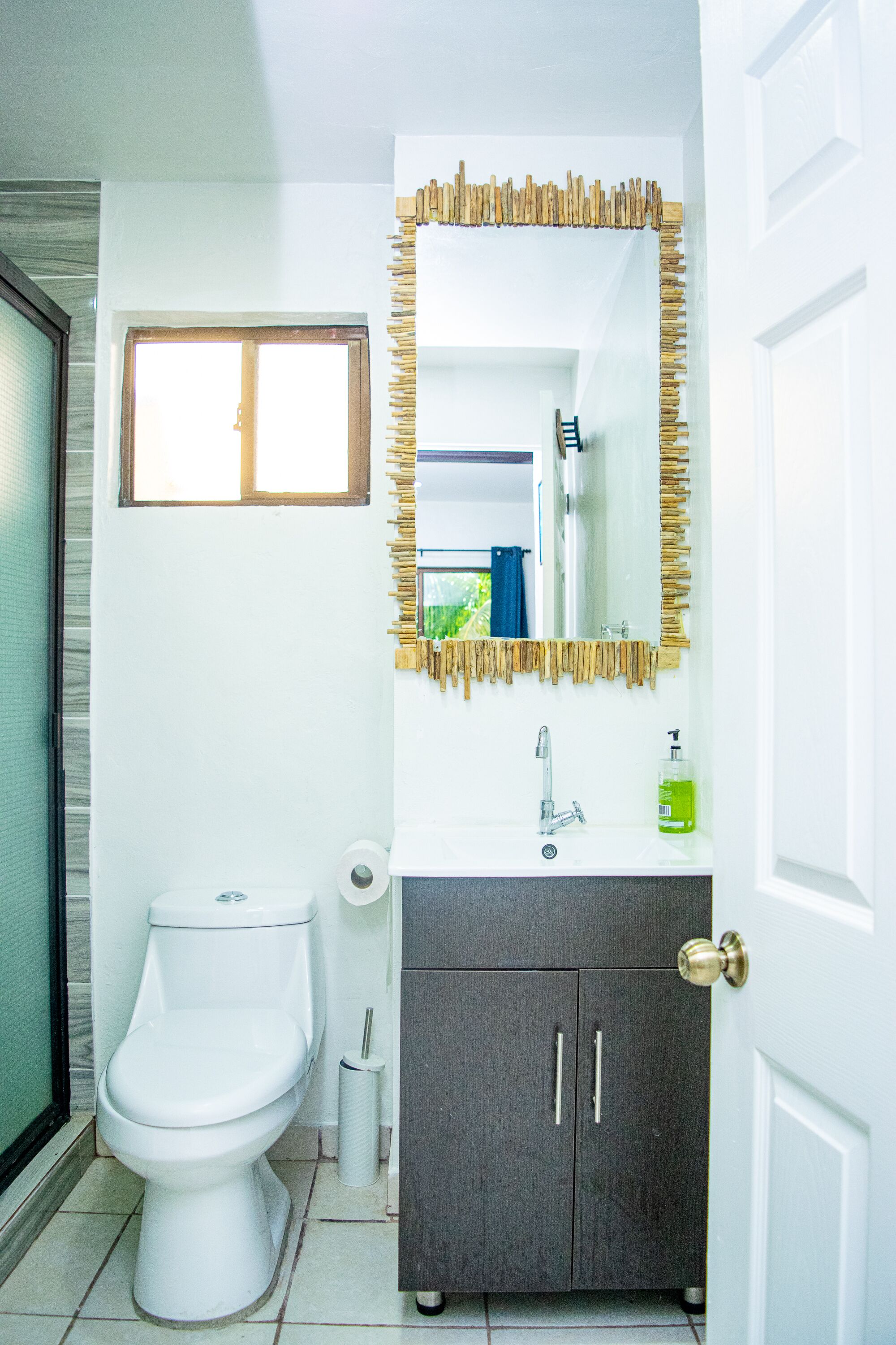 Un baño con inodoro, lavamanos, espejo y un armario.