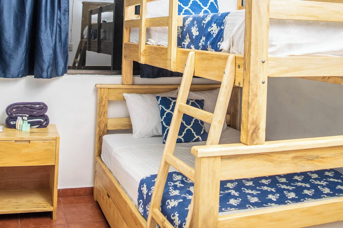 A bunk bed room with a wooden frame, a small table, and a window with curtains.