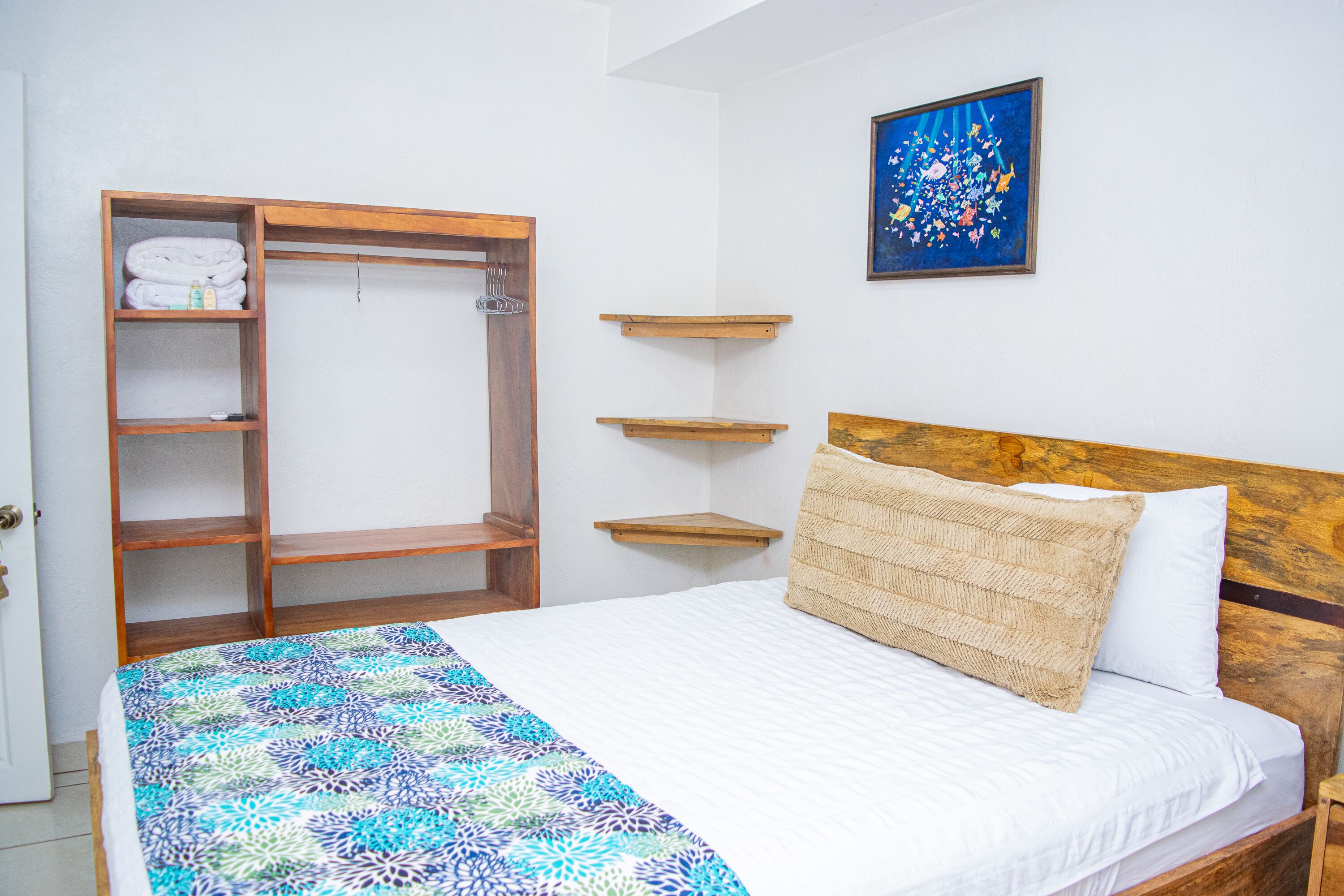 A bedroom with a bed, a wooden wardrobe, and a wall-mounted shelf.