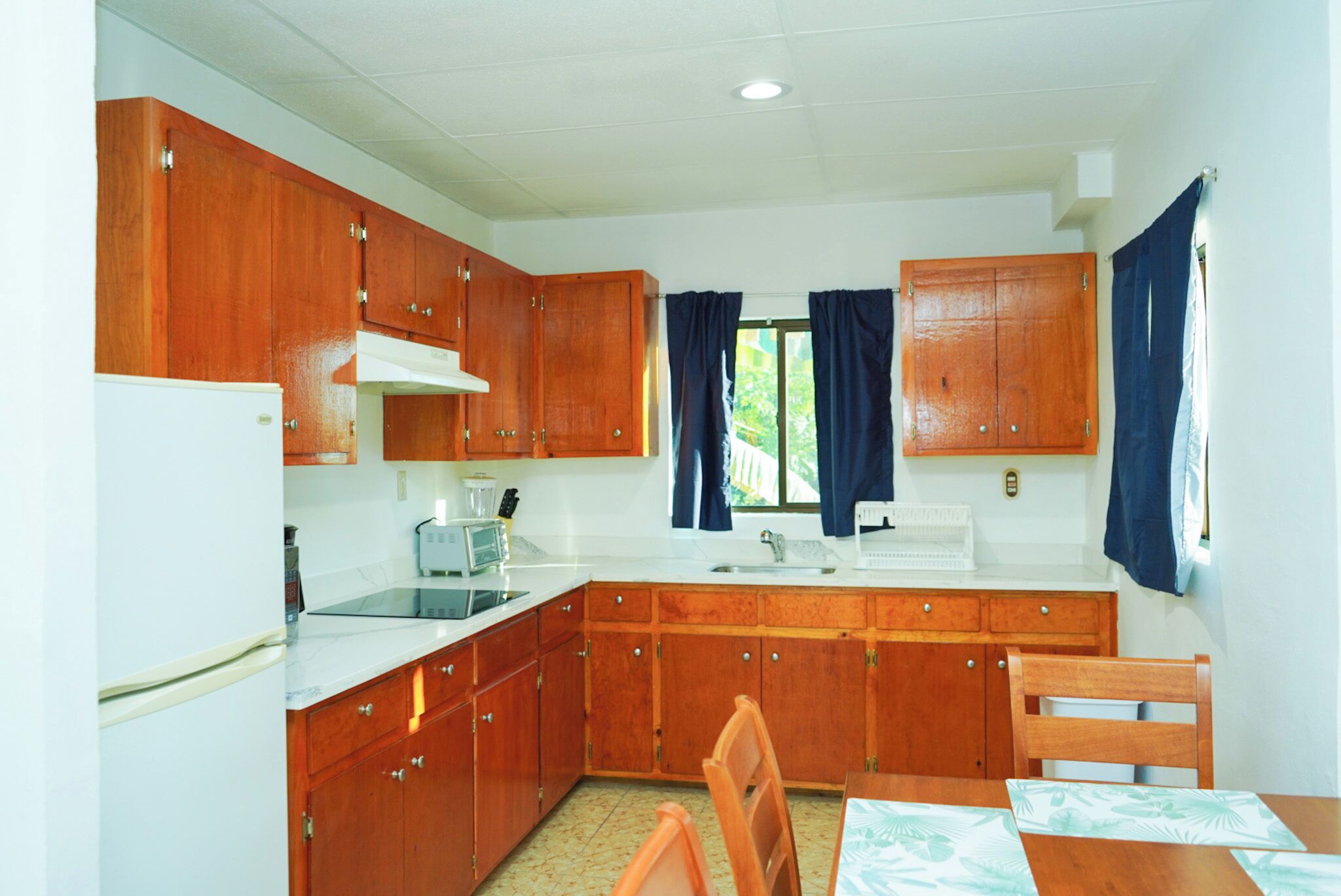 Una cocina compacta con armarios de madera, una encimera blanca, un lavabo y un comedor con mesa y sillas.