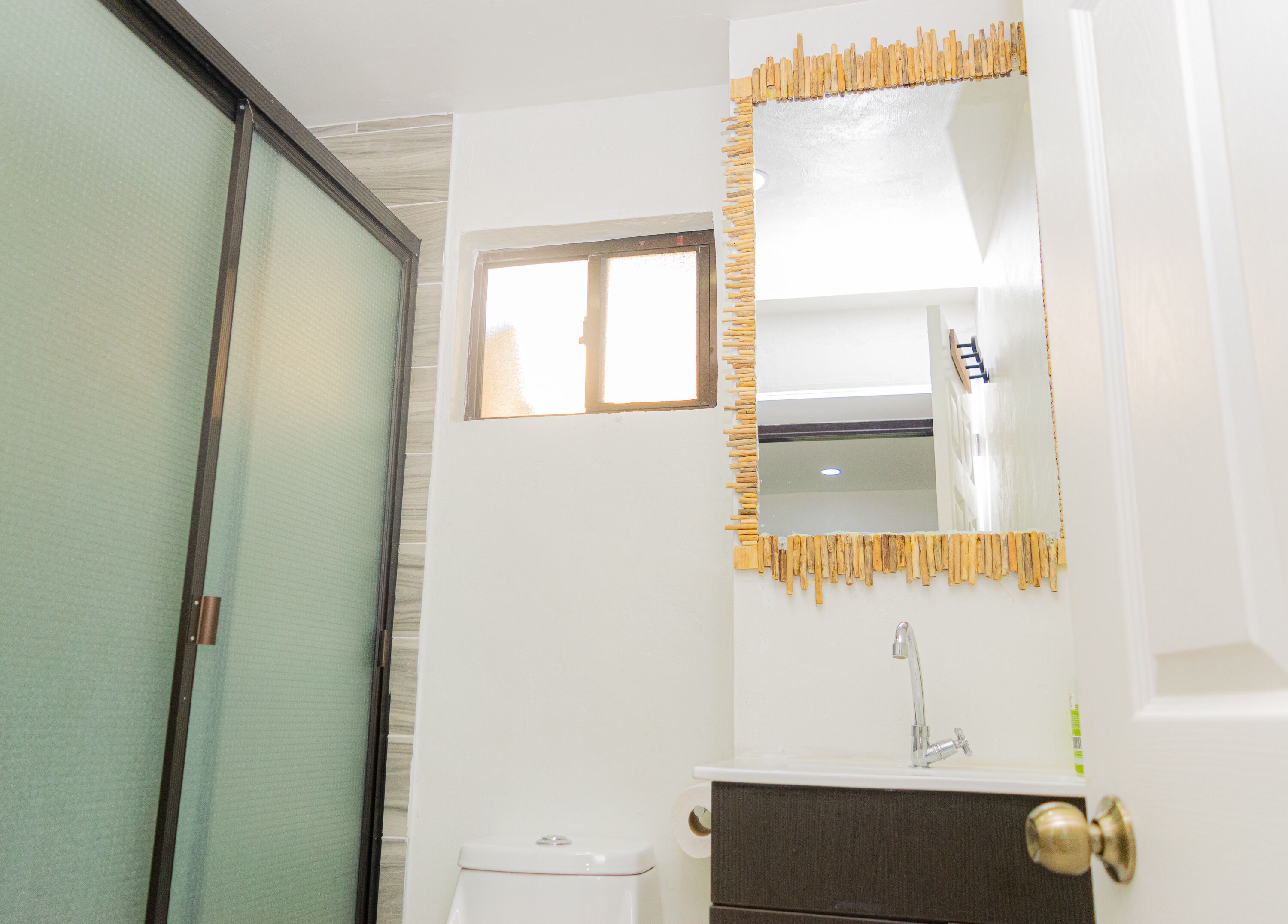 Un baño con inodoro, lavamanos, espejo y ventana.