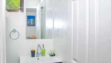 Un bagno con lavandino bianco, mobile contenitore in legno scuro, uno specchio e una porta.