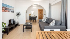 A modern living room with a sofa, coffee table, TV, and a dining area with chairs and a table.