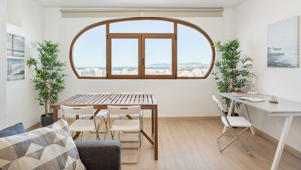 A modern living room with a wooden dining table, two white chairs, a sofa, and two potted plants.