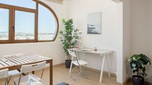 A modern apartment with a large window, a white desk, a potted plant, and a view of the city.