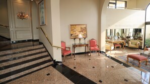 A spacious lobby with a grand staircase, a seating area with chairs, a table, and a large painting on the wall. - 4 BR Oceanfront Oasis: Luxury Amidst the Bustle w Heated Pool & Private Balcony (South Padre Island)