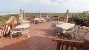 A wooden deck with outdoor furniture, including tables and chairs, overlooking a beach. - 4 BR Oceanfront Oasis: Luxury Amidst the Bustle w Heated Pool & Private Balcony (South Padre Island)