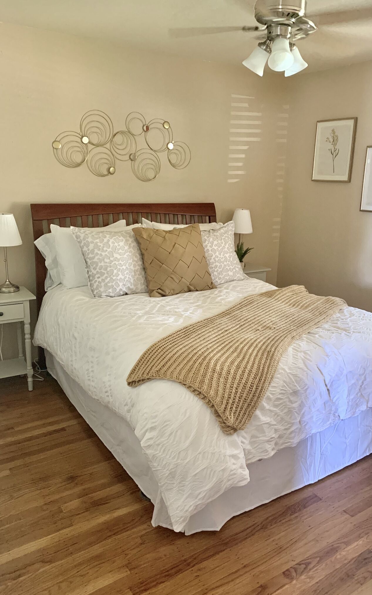 Un dormitorio con cabecera de madera, ropa de cama blanca, una manta color beige y una lámpara de pared.