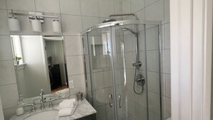 Un baño moderno con ducha envuelta en vidrio, lavamanos con espejo y muebles de tonos oscuros.