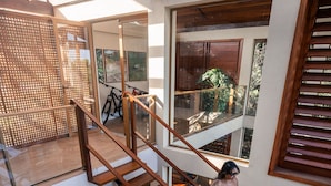Eine mehrgeschossige Holztreppe mit Glasgeländern, die zu einem Balkon mit Ausblick ins Freie führt.