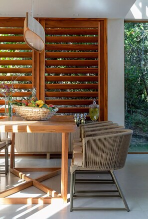 A dining area with a wooden table, wicker chairs, and a fruit basket. - Casa Oceano- Praia do Forte (Açu da Torre)