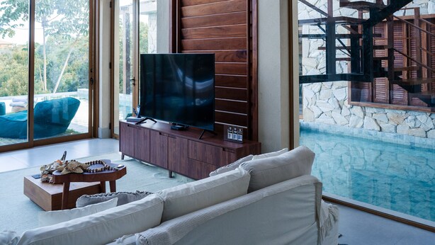 Ein modernes Wohnzimmer mit großem Fernseher, weißem Sofa und Blick auf einen Pool.