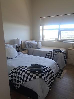 A bedroom with two beds, a nightstand, a lamp, and a window with a view.