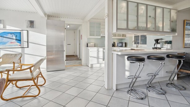 Una cocina moderna con armarios blancos, una isla central con taburetes y un comedor con sillas de mimbre.