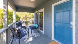 Un portico coperto con due sedie e un tavolo, una porta blu e vista sul verde.