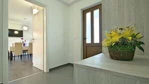Ein Flur mit einer Holztür, einem Blumentopf mit gelben Blüten und einem Essbereich im Hintergrund.