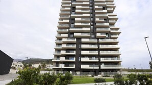Un immeuble moderne de grande hauteur, doté de nombreux balcons, d’une façade plane et entouré d’un espace paysager aménagé.