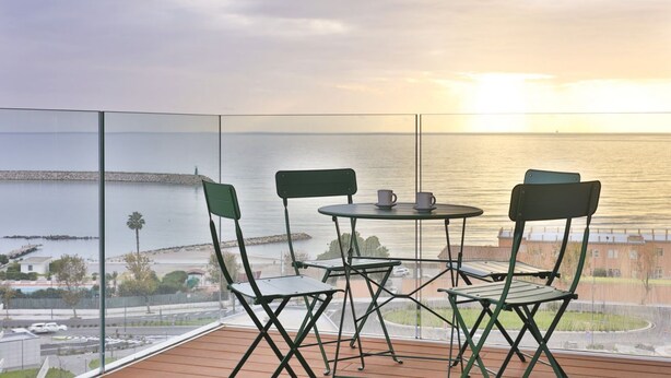 Un balcon avec une table et des chaises, donnant sur une étendue d’eau et une côte lointaine.