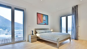 Une chambre à coucher avec un lit, une table de chevet, un tableau et de grandes fenêtres donnant sur la ville.