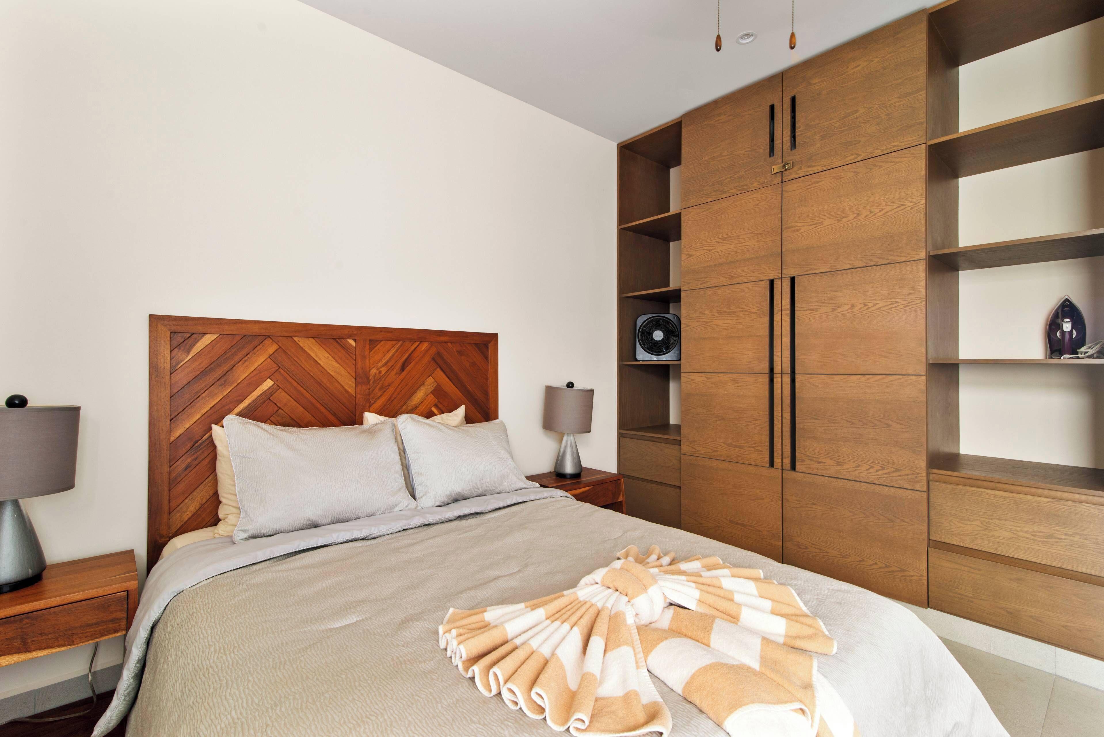 Una camera da letto con una testiera in legno, un letto con coperta a righe, un comodino con una lampada e mensole incorporate in legno.