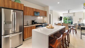 Una cucina moderna con frigorifero in acciaio inossidabile, mobili in legno, un'isola centrale con sgabelli da bar, forno integrato e microonde.