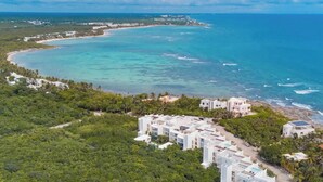 Vue aérienne d’une station balnéaire comprenant plusieurs bâtiments, une plage et des eaux turquoise cristallines.