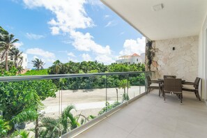 Un balcon équipé d’un ensemble de mobilier de jardin et offrant une vue sur une plage et une végétation luxuriante.