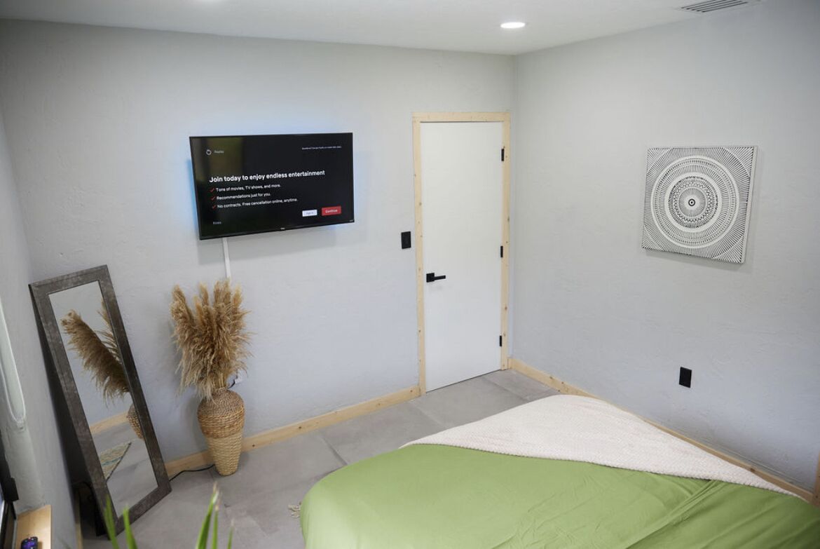 Une chambre à coucher comprenant un lit, un téléviseur fixé au mur, une porte et un élément décoratif mural.